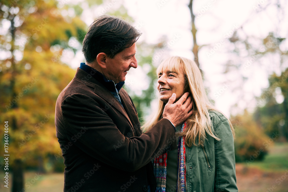 Fototapeta premium Senior couple sharing a tender moment, man's hand caressing woman's face, in an autumn park