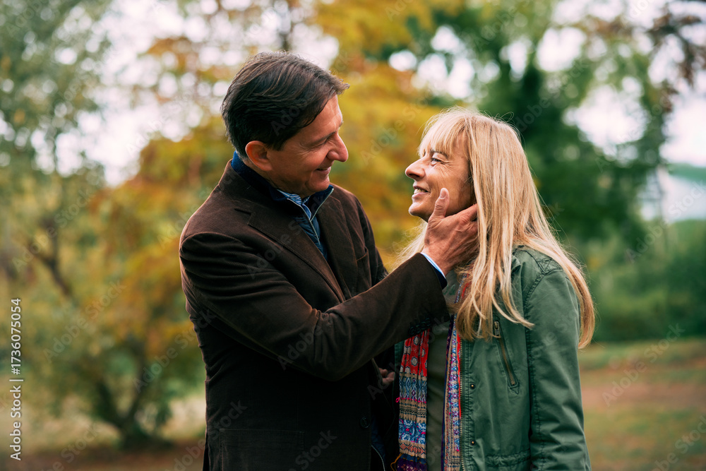 Fototapeta premium Mature couple showing affection during a walk in the park surrounded by autumn colors