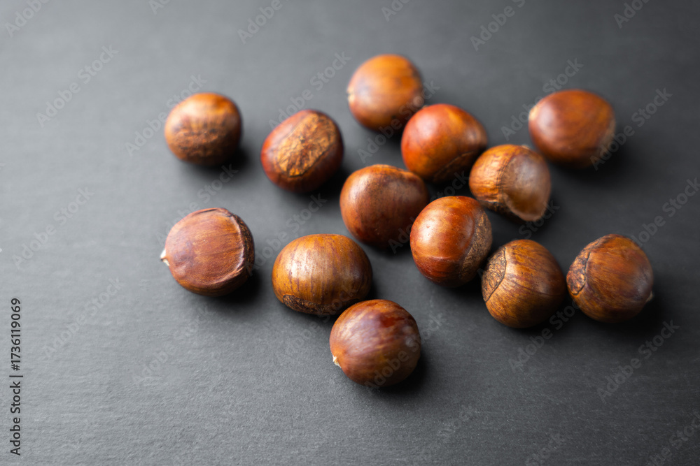 Obraz premium Raw chestnuts scattered on dark background, organic autumn nuts with natural brown shells, healthy seasonal food rich in nutrition, perfect ingredient for cooking, roasting,