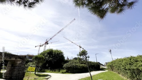 construction site with multiple cranes is seen rising above a green landscape filled with trees and