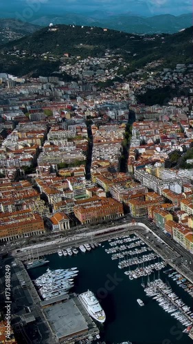 Epic 4K vertical aerial video of Nice harbor with luxury yachts, marina, and Alpine mountains. Stunning drone footage capturing French Riviera port with terracotta rooftops, perfect for mobile reels.