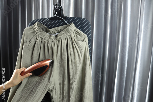 modern black and golden steam iron for ironing clothes steam is used by left hand to iron with brown long pants dress with background of grey curtain in laundry room before putting for working in 