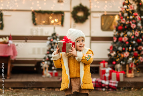 little girl looks up and waits for the first snow and celebrates Christmas near the trailer with Christmas decorations