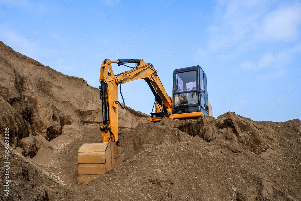 Obraz premium Construction site on a sunny day. Industrial excavator digging sand to lay the foundation for a building. Workers operate the excavator.