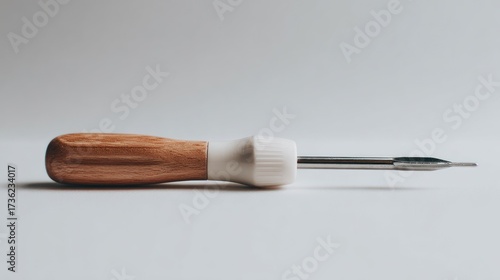 A light-colored screwdriver with a wooden handle lies on a plain white background