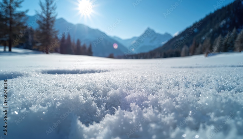 Obraz premium Close-up photo showcases snow texture. Bright sun shines above the snowy landscape. Background reveals mountains trees and clear blue sky. Scenic winter day outdoor adventure scene.