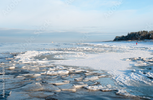 Frozen Winter Shoreline with Snow and Ice.Scenic cold weather seascape with icy textures and a distant figure on the snowy horizon.