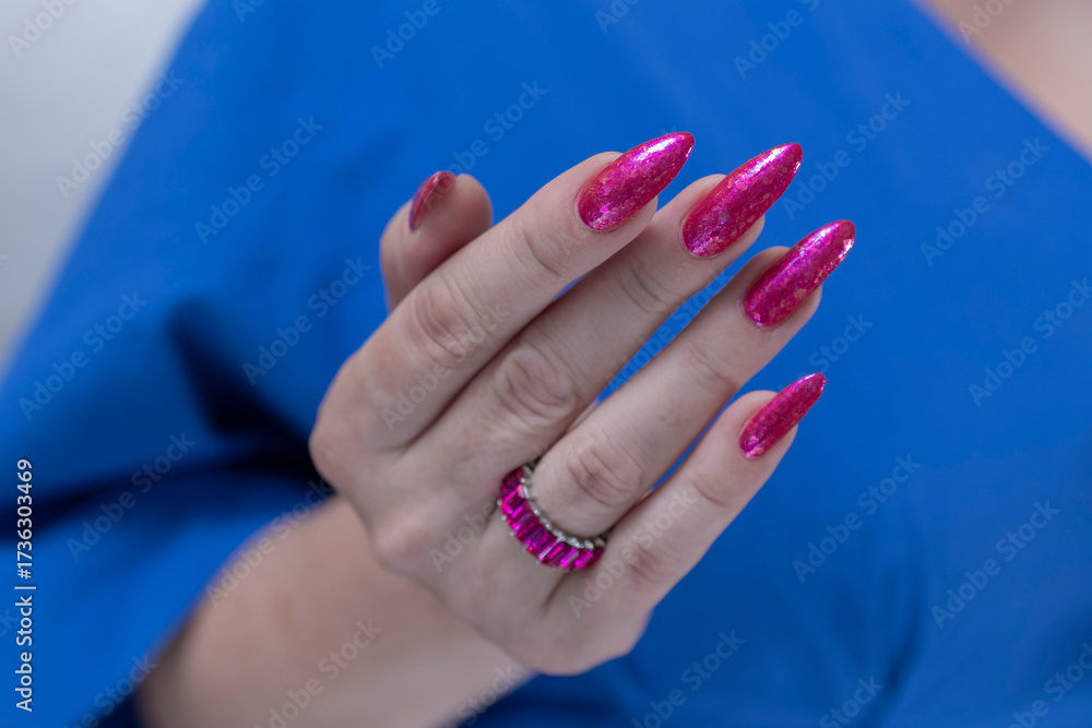Fototapeta premium Female hand with long nails and a bottle bright neon pink fuchsia color nail polish