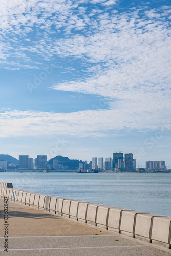 Scenic view of the waterfront promenade at Esplanade, George Town, Penang, Malaysia. The modern city skyline with high-rise buildings, calm sea, and blue sky creates a vibrant urban coastal landscape.