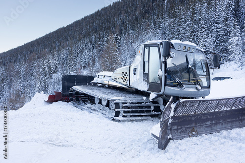 Canvas Print Snow-covered snowcat vehicle parked on a mountain slope, surrounded by evergreen