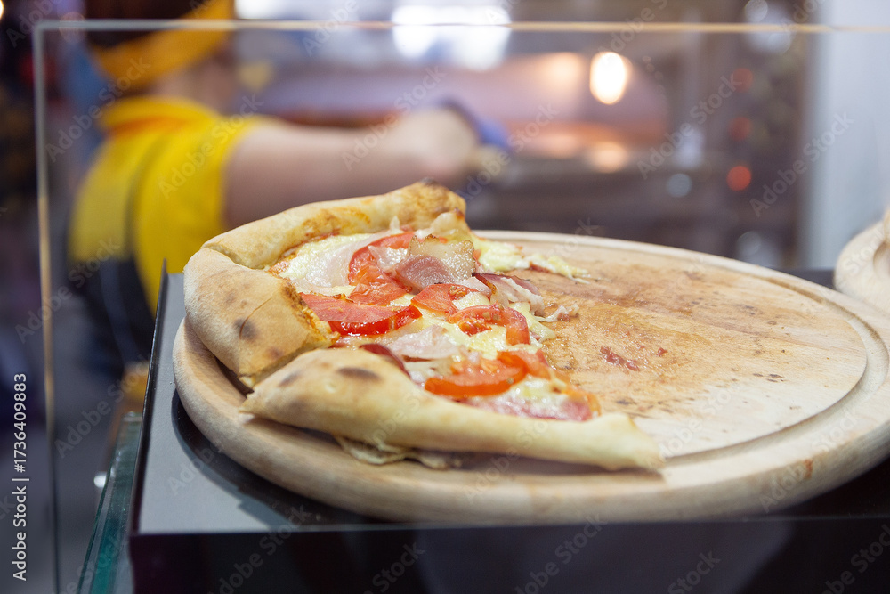 Obraz premium Pizza in the pizzeria window and cook near the oven in the background