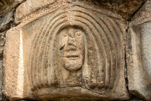 Close-up of a weathered stone capital from the Romanesque church of Sant Lliser d'Alós d'Isil, carved with a primitive, stylized human face. Catalonia, Spain.
