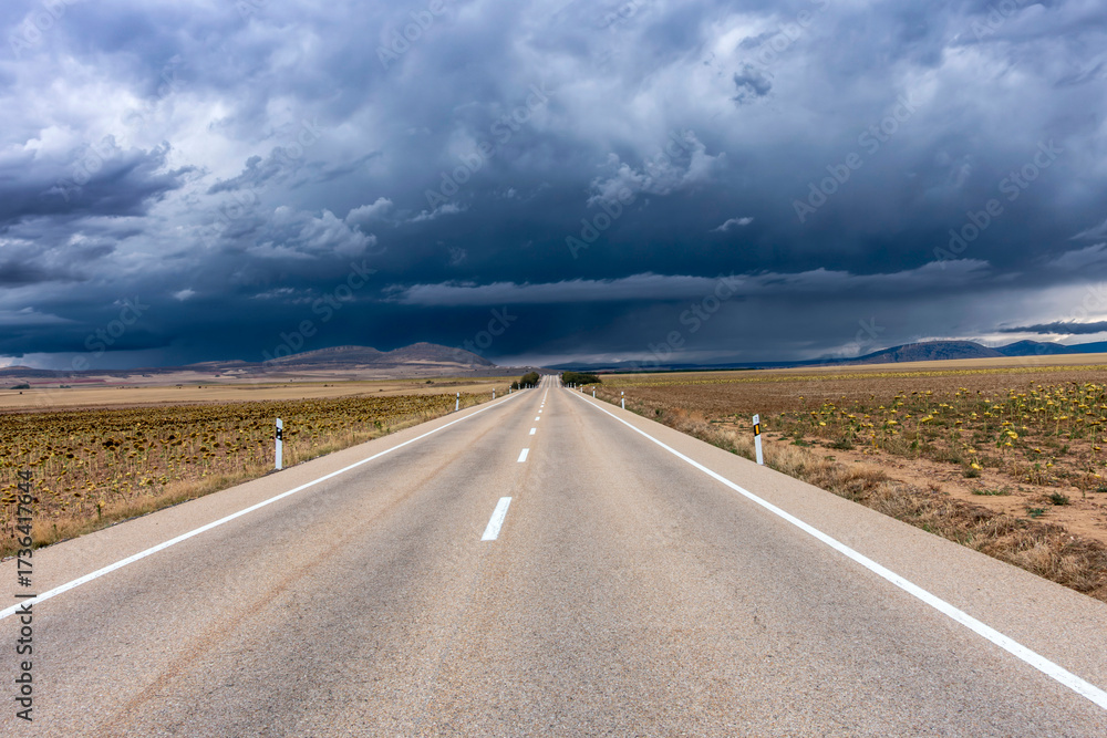 Naklejka premium Journey through the Comarca de Campo de Gómara: An empty road leads into a dramatic storm in rural Spain.