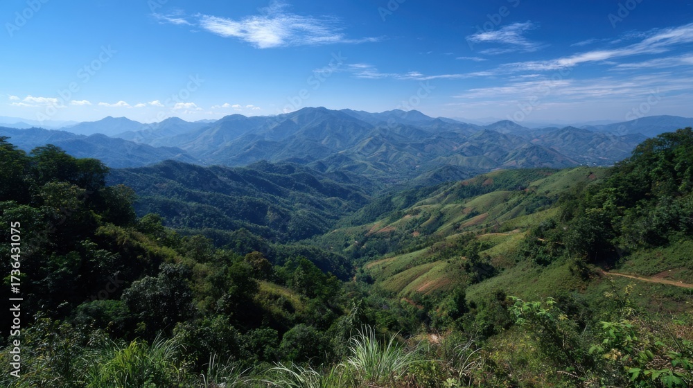 Obraz premium Lush green hills stretch across the horizon in a stunning mountainous landscape. The vibrant valleys create a serene atmosphere, framed by a bright blue sky with wispy clouds.