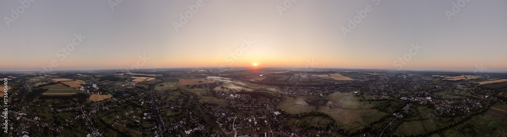 Obraz premium Wide view of dawn in Ukrainian countryside with glowing sun, rural village and farmland