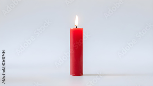 A single red candle stands lit against a plain white background, its flame casting a soft glow and creating a serene and minimalist composition.