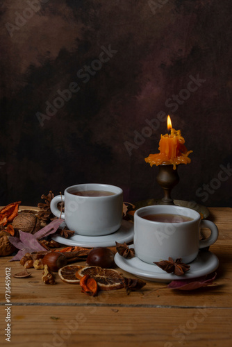 Close-up of two cups of tea on a wooden table with nuts, leaves, and a lit candle, vertically with copy space