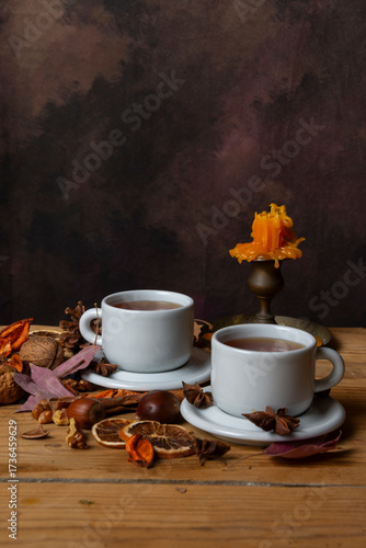 Close-up of two cups of tea on a wooden table with nuts, leaves, and an unlit candle, vertically with copy space