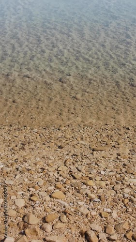 Clean water in Dead Sea, you can see the sandy bottom and small stones there. Covered stones with salt on the deep. Smoothly backward shot with Steadicam. Vertical video