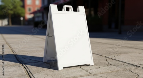 Blank white a frame sign standing on a paved sidewalk with buildings in the background