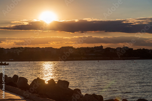 Stunning sunset over the calm sea, with warm golden and orange hues reflecting on the water. The peaceful coastal scene evokes relaxation, romance, and natural beauty, perfect for themes of travel, 
