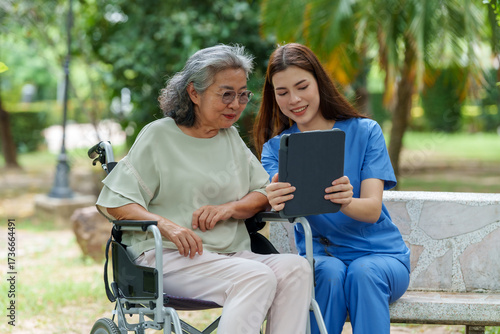 Caring caregiver provides assistance and support to senior in wheelchair while using tablet outdoors, showcasing importance of companionship in care