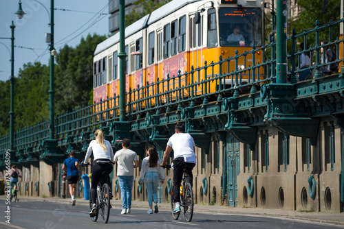 People biking and walking against old tram on overpass