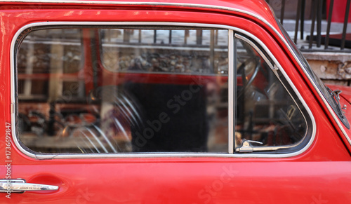 Fototapeta Naklejka Na Ścianę i Meble -  side view of detail small red retro historical aged vintage old oldsmobile motor car is parked on a quiet street against stone wall
