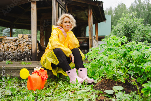 Woman gardening in raincoat beside flourishing plants