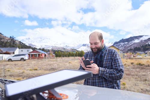 Man connecting to Wi-Fi from a remote village using a satellite internet antenna. Technology allows travelers to stay connected while traveling.