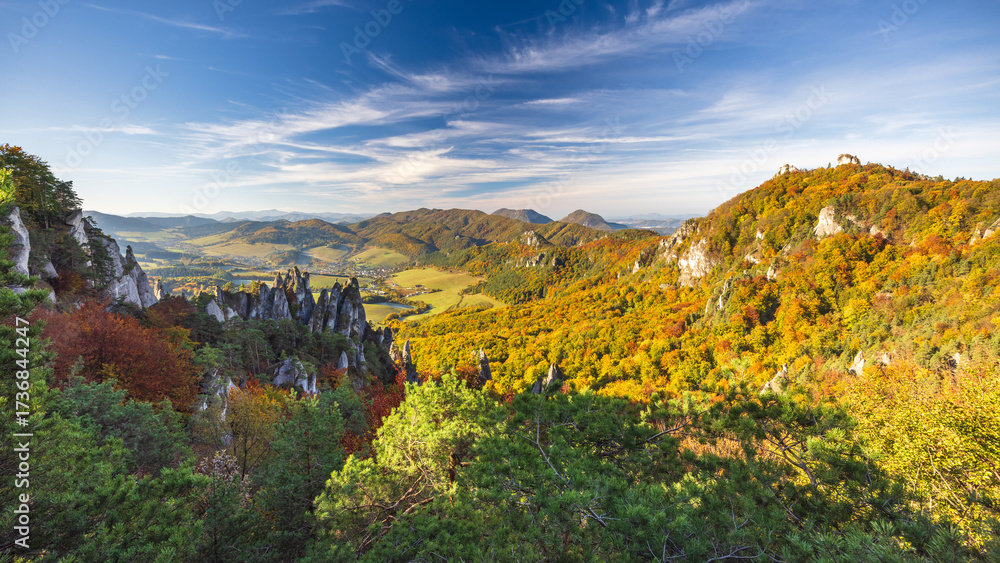 Fototapeta premium Scenic autumn landscape featuring rocky outcrops, vibrant foliage, rolling hills, and a wispy blue sky, perfect for exploration. The Sulov Rocks, national nature reserve in Slovakia, Europe.
