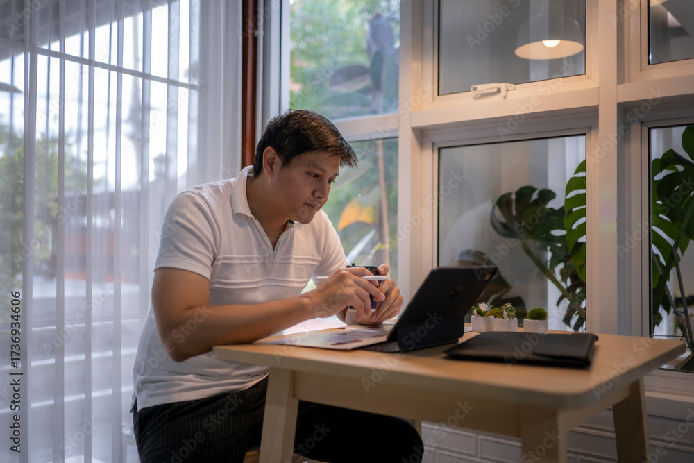 Obraz premium Asian freelancer working from home using tablet and drinking coffee