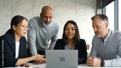 A multicultural group of professionals engaged in a collaborative team meeting, discussing a project on a laptop in the office