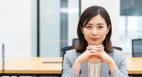 オフィスで手を組み笑顔を見せている、信頼感のある20代日本人女性社員