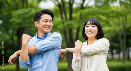 Smiling asian couple stretching arms in a green park