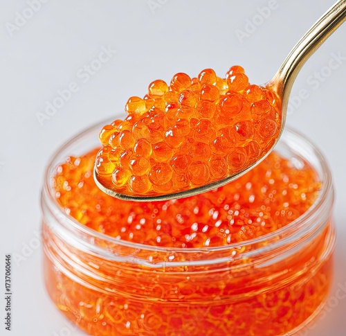 Golden spoon holds bright orange caviar over a glass jar