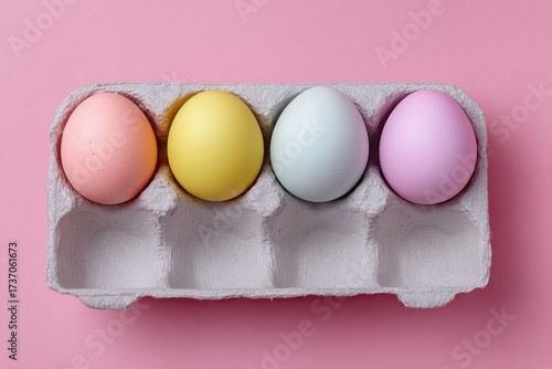 Four pastel-colored eggs rest in a carton, on a pink background