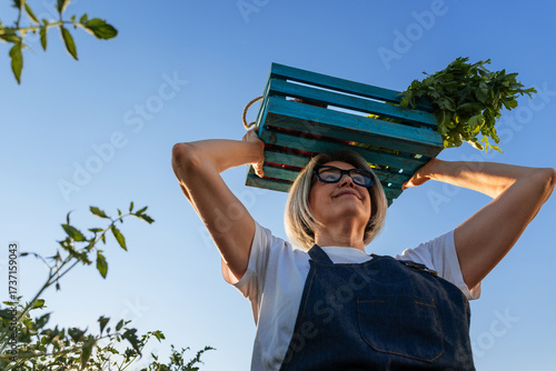 Female farmer carrying crate of vegetables on head in cultivated field
