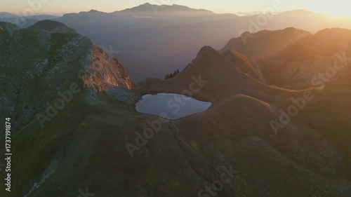 Drone video of the alpine lake Drakolimni Tymfis surrounded by mountain peaks at sunrise. Stunning natural scenery perfect for travel, adventure, and documentary projects.