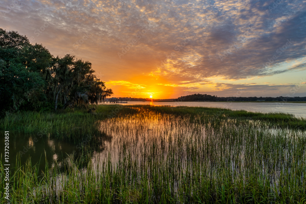 Obraz premium Sunset over serene marshland reflecting bright hues in the water at golden hour near a quiet riverside