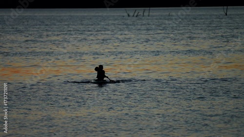 silhouette of young kayaker paddling on a lake at dusk