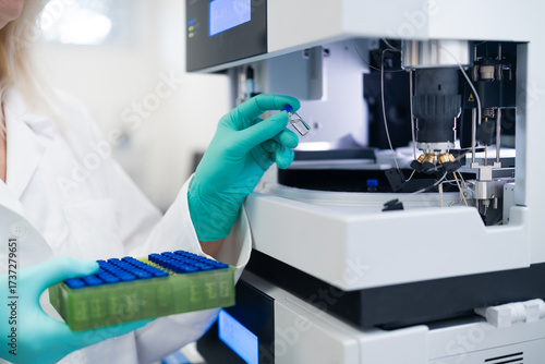 Scientist in rubber gloves carefully loading vial into autosampler for chemical, pharmaceutical, and clinical testing procedures