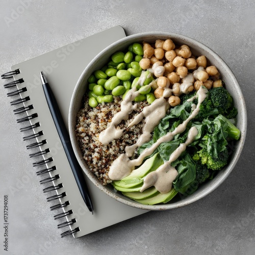 Healthy vegan buddha bowl with quinoa, vegetables, and tahini dressing on notebook