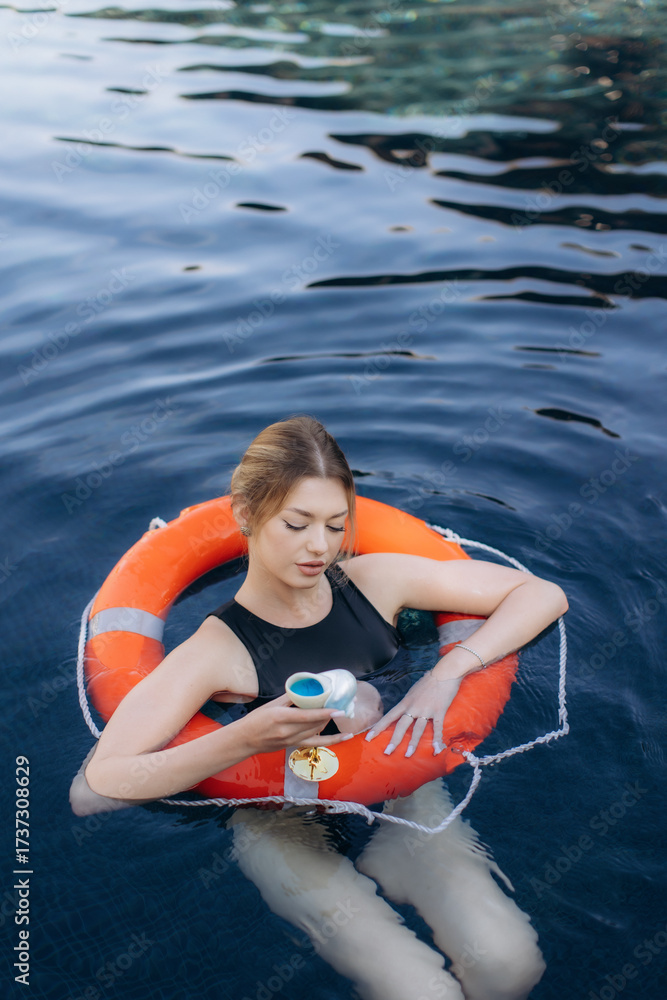 Obraz premium Young woman relaxing in swimming pool with lifebuoy and cocktail