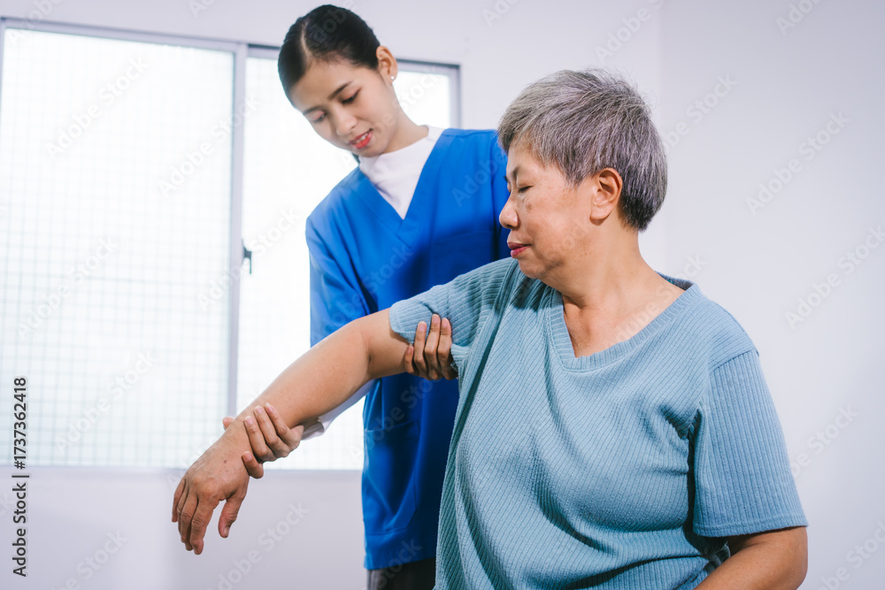 Fototapeta premium An Asian female nurse provides caring home care to an elderly woman, assisting with arm movement exercises, physical therapy,and rehabilitation to improve joint function, strength,overall well-being