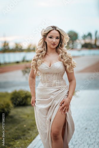 Radiant caucasian woman in a champagne satin prom dress with a high slit, posing outdoors