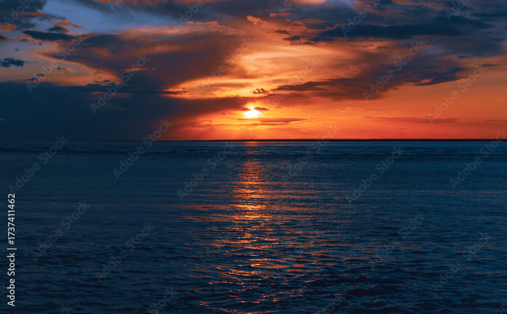 Obraz premium Vibrant sunset over calm ocean waters with colorful clouds reflecting on the surface