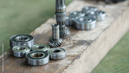 A collection of metal ball bearings and bevel gears laid out on a worn wooden surface, likely in a workshop or repair setting.