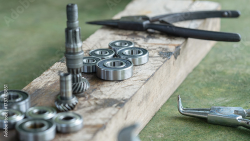 A collection of metal ball bearings and bevel gears laid out on a worn wooden surface, likely in a workshop or repair setting.