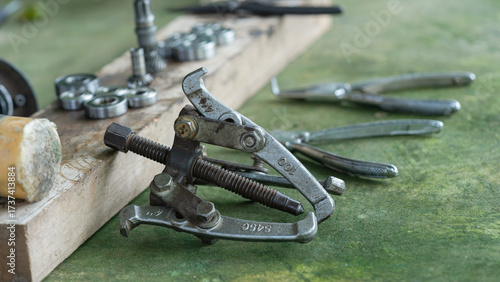 A metal bearing puller tool on a workshop table with pliers and ball bearings, used for mechanical maintenance and engineering tasks, essential for disassembly and repair of machinery components.